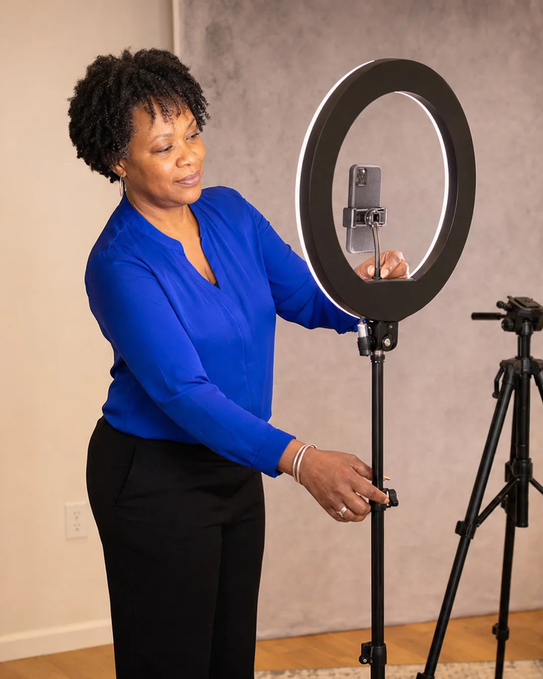 A creator adjusts a large ring light and phone mount in a warm home studio
